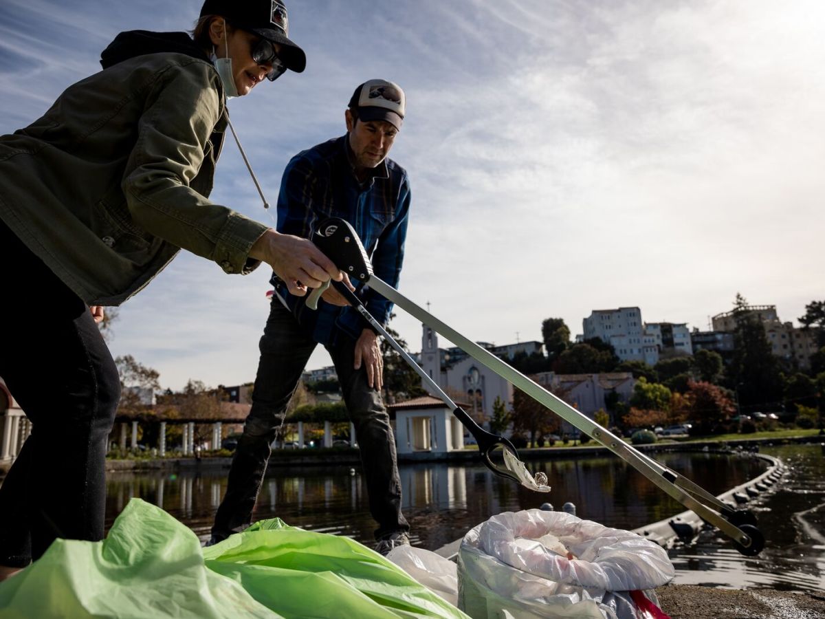 two people picking up trash from Lake Merritt with trash pickers.