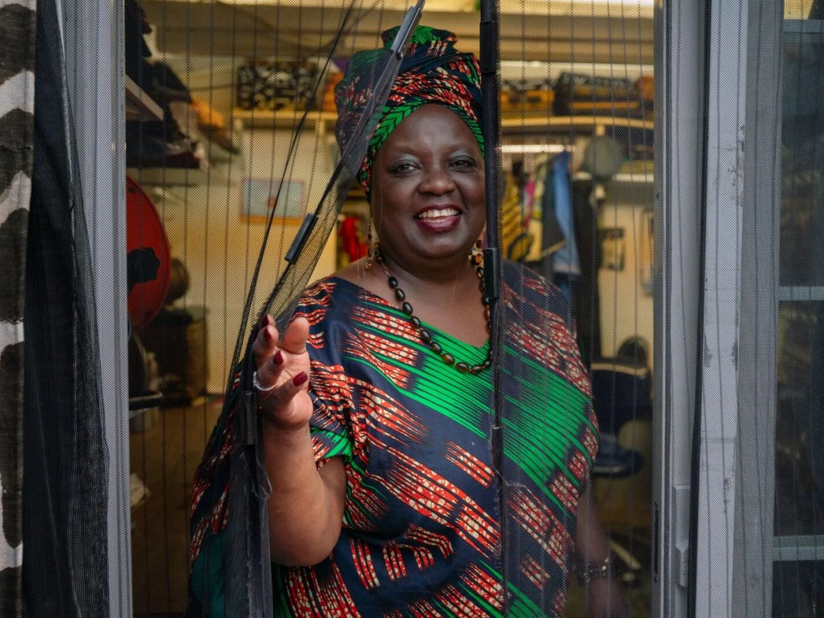 A woman wearing a red, green, and navy dress and matching headwrap smiles.