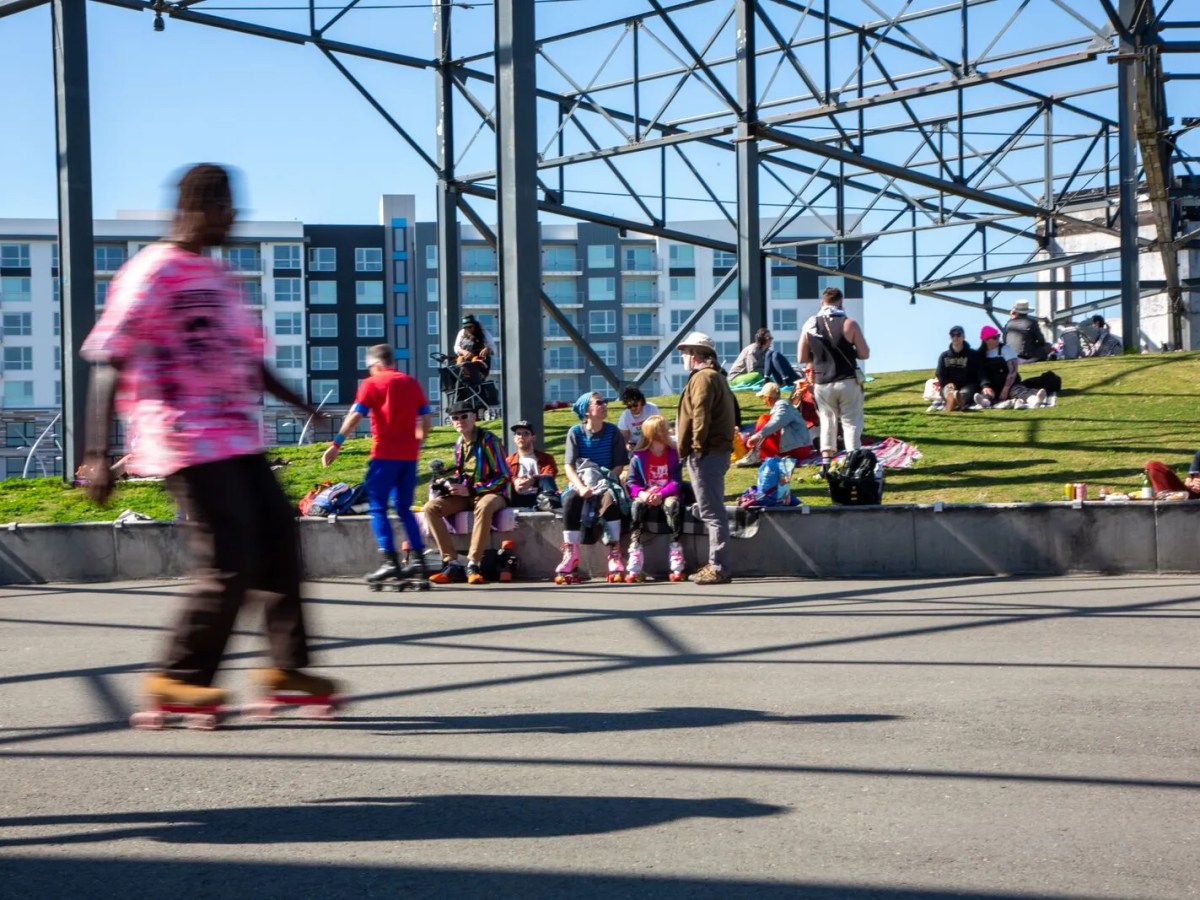 A crowd watches a man rollerskating at an urban park.
