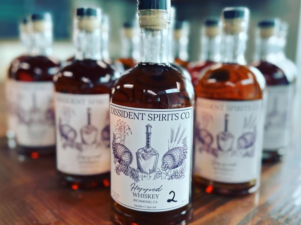 Bottles of liquor from Dissident spirits are lined up in a triangle shape on a wooden countertop.