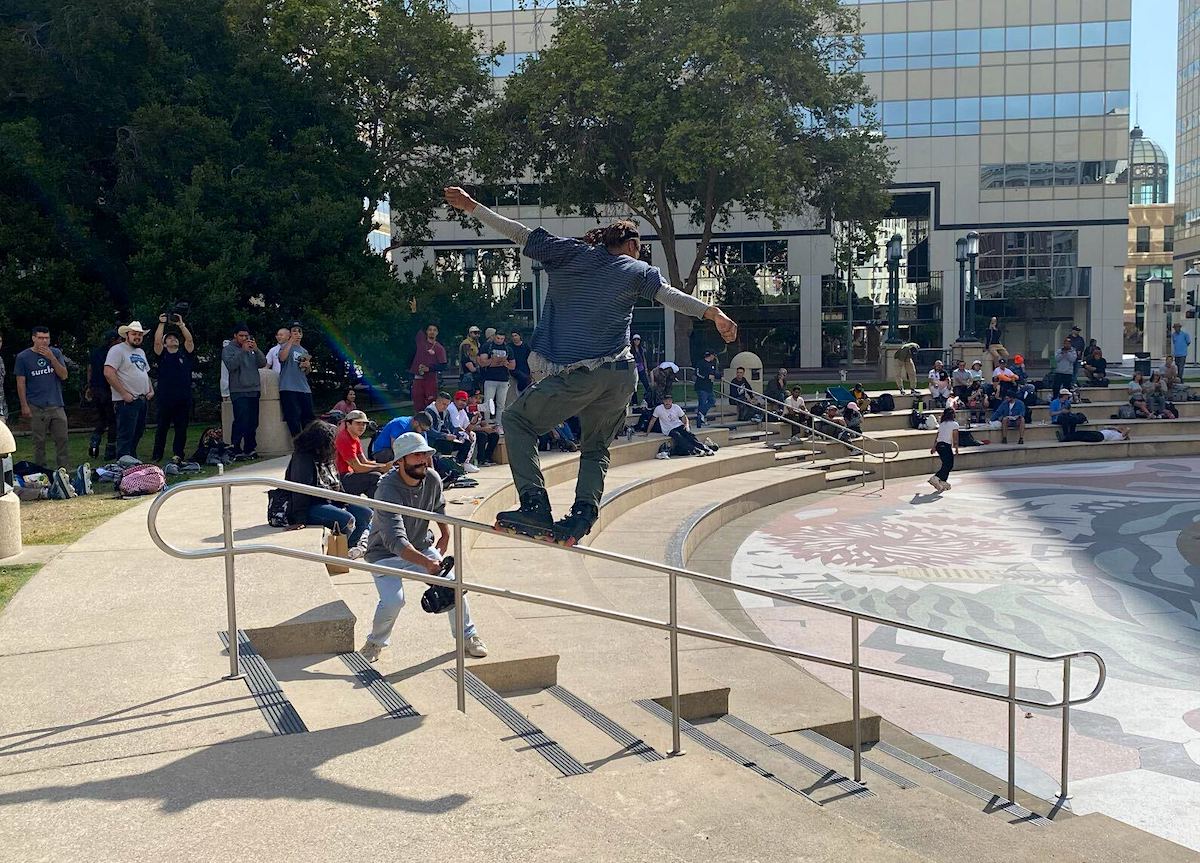 A rollerblader slides down a handrail outside Oakland City Hall while a crowd of onlookers watch in awe.