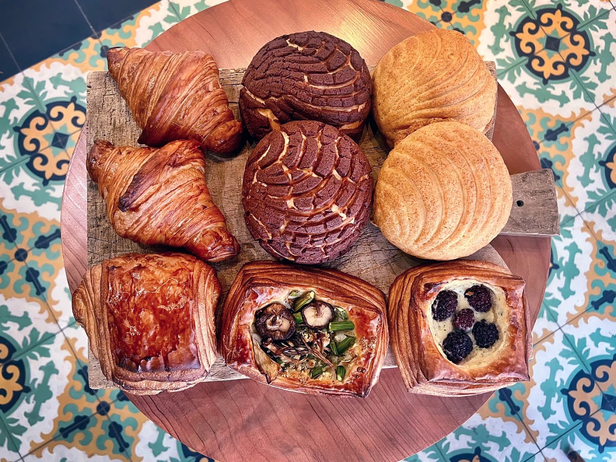 A selection of pastries from Forma Bakery, including croissants and conches, sit on a wooden plate with a background of mosaic tiles.