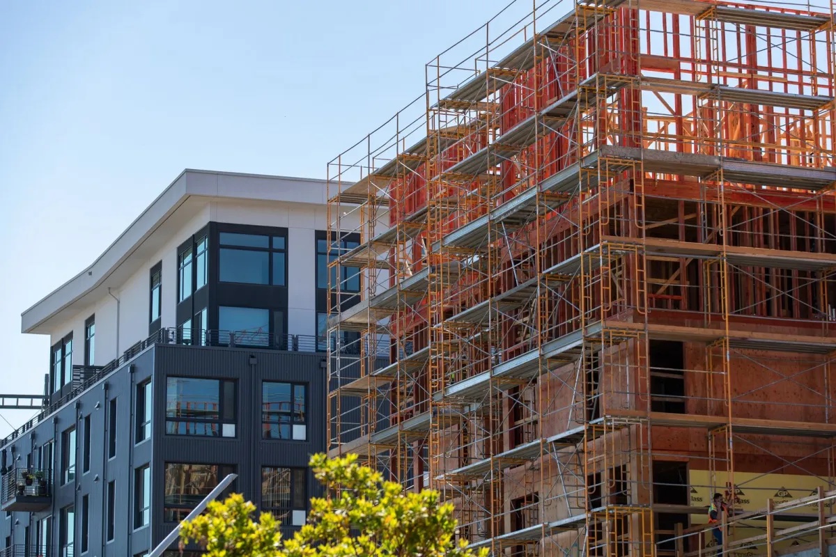 A wood-framed apartment building under construction next to a new, finished building.