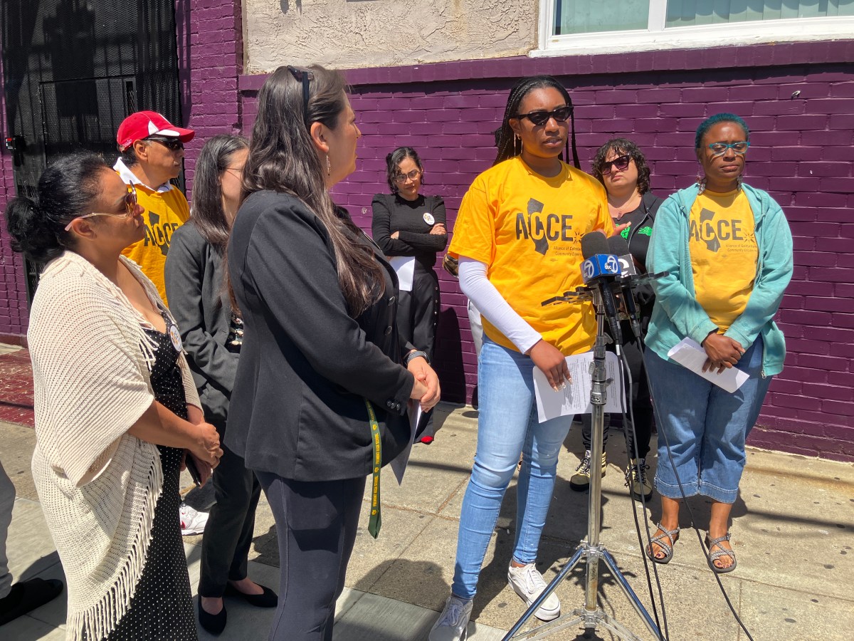 About 10 people, some in matching shirts, speak in front of news microphones.