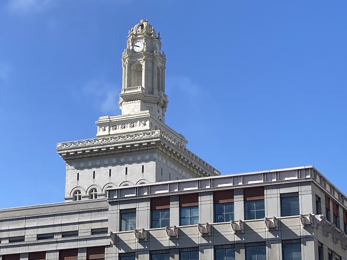 The top of Oakland City Hall visible above a city office building, all framed by the bright blue sky.