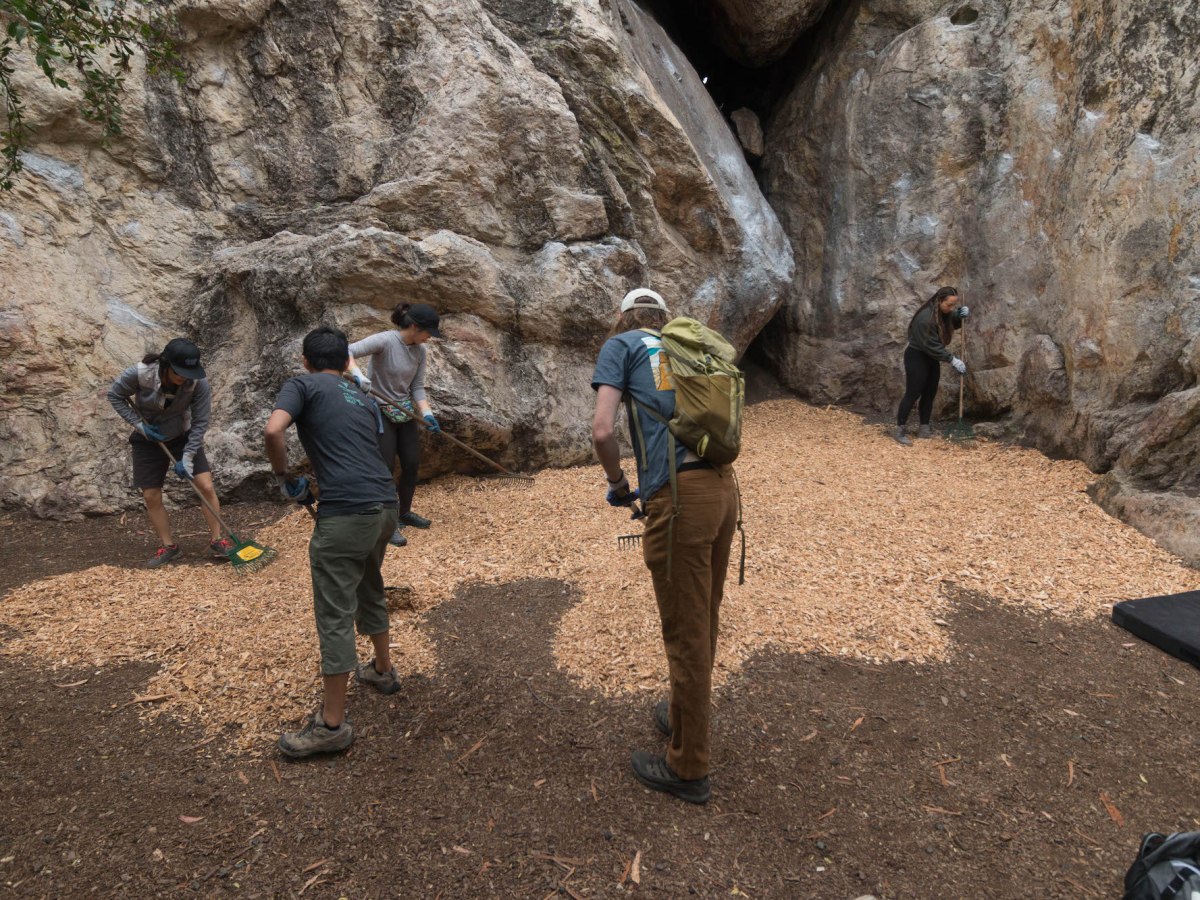 Two people cleaning up a area at the base of a outdoor bouldering wall