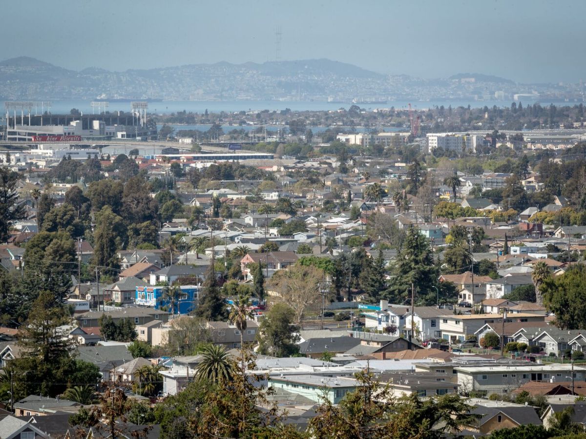 The skyline of a dense neighborhood with a scattering of trees and a bay in the distance.