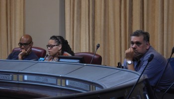 Two men and a woman sit behind a dais with microphones in front of them.