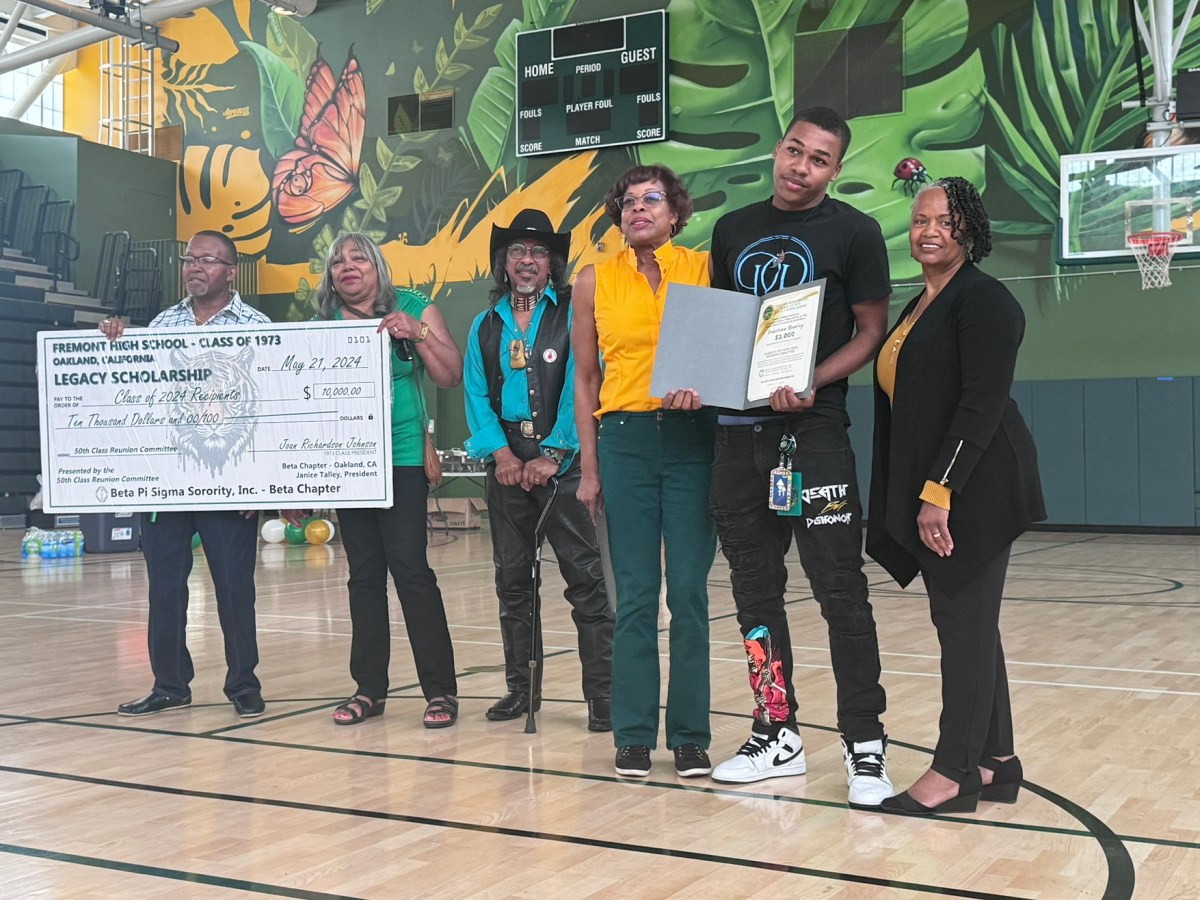 A young man proudly holds up a set of papers awarding him a scholarship. Beside him stand members of the Fremont High School Class of 1973 who raised money for the scholarship.