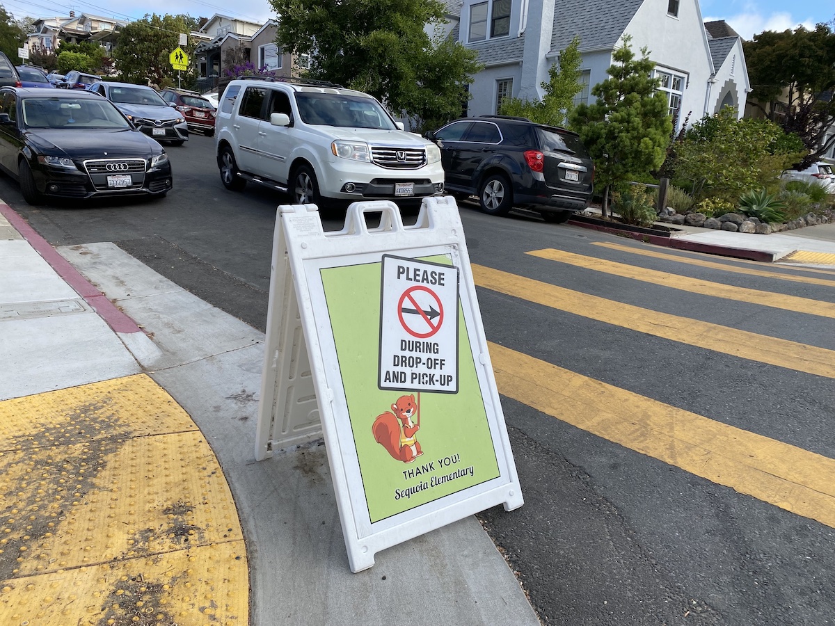 A sign tells cars how to pick up and drop off students outside an Oakland school.